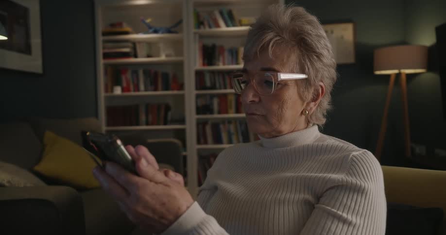 Lady sitting down on a yellow couch reading from a bank card and typing on a smartphone indoors during day time