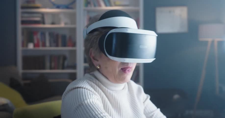 A female in a dark living room with flashing lights is wearing a virtual reality headset while moving her arms in the air