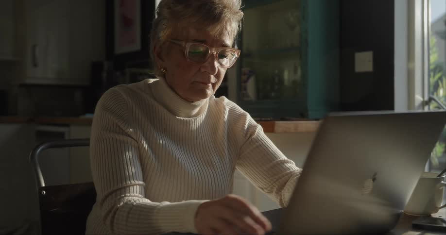 Close up of an elderly woman using a laptop computer while sitting a table indoors during daytime