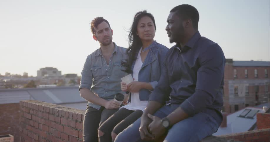 People sit on a ledge on a rooftop and talk