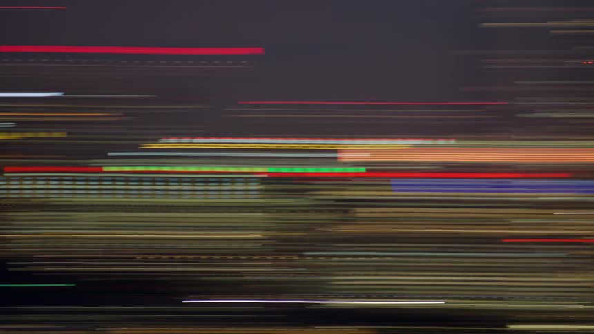 An abstract time lapse shot captures streaks of golden red and blue light moving rapidly across a dark background suggesting movement at high speed through a city at night