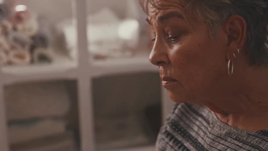 An older woman rocks a swaddled infant in her arms as she sits in a rocking chair in a room