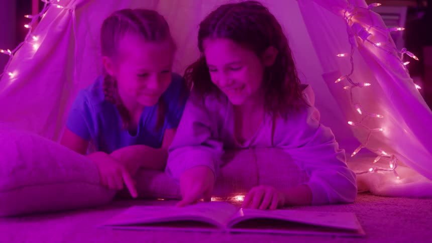 Children reading a book inside a tent lit by colored lights