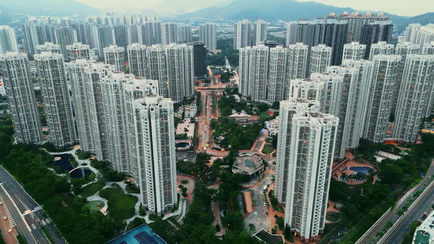 A densely packed urban landscape featuring dozens of towering residential highrises revealing a central corridor of green parkland and connecting roads between the buildings with distant mountains