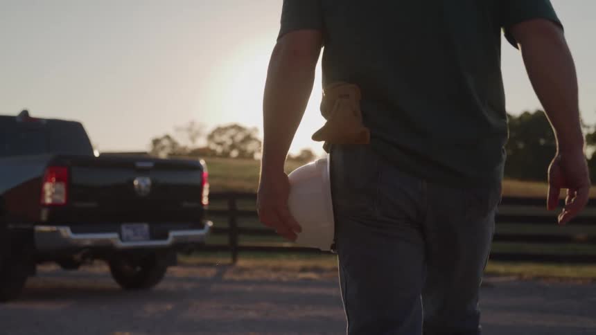 A man holds a hardhat as he walks toward a pickup truck