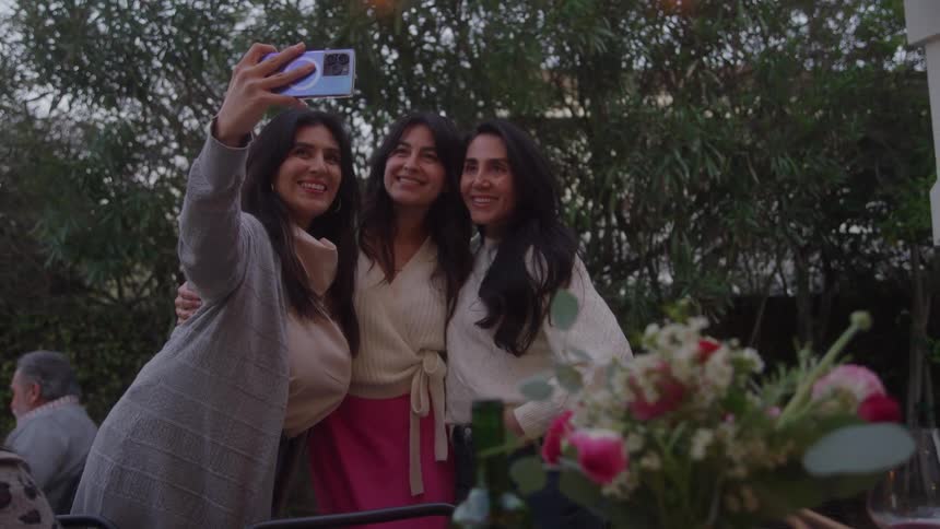 Three women take a selfie while attending an outdoor family event on an autumn day