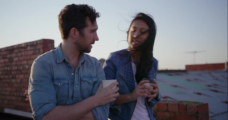 A man and woman drink coffee on a rooftop