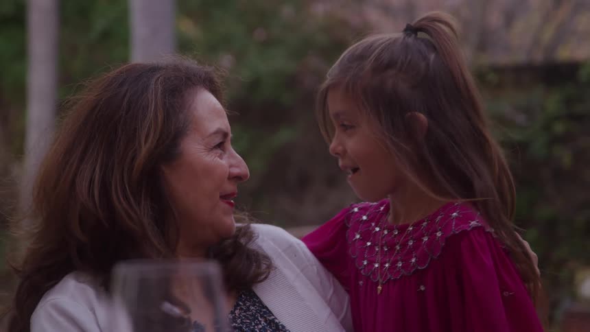 Grandmother and granddaughter smile at each other and lean their foreheads together as they sit outdoors and talk