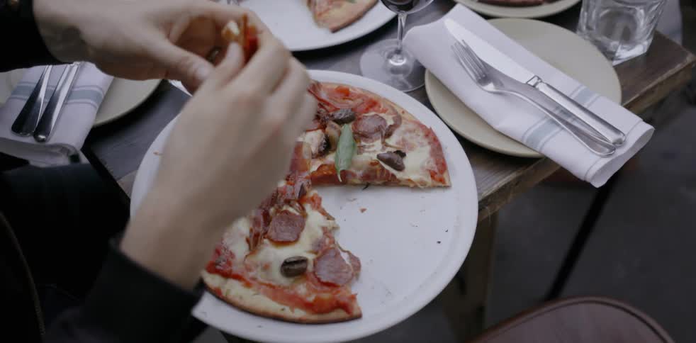 Two people sitting at table outdoor eating pizza