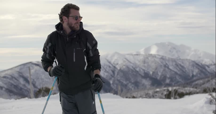 A man skiing in the snow with mountains behind him