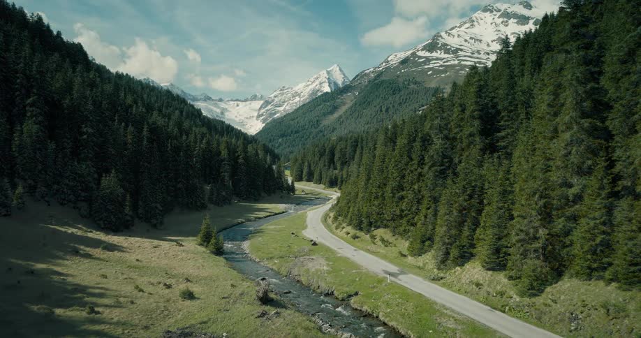 Aerial view of snow covered forested mountains with a road running through the valley next to a stream with snow melting and then the sun shining in the spring