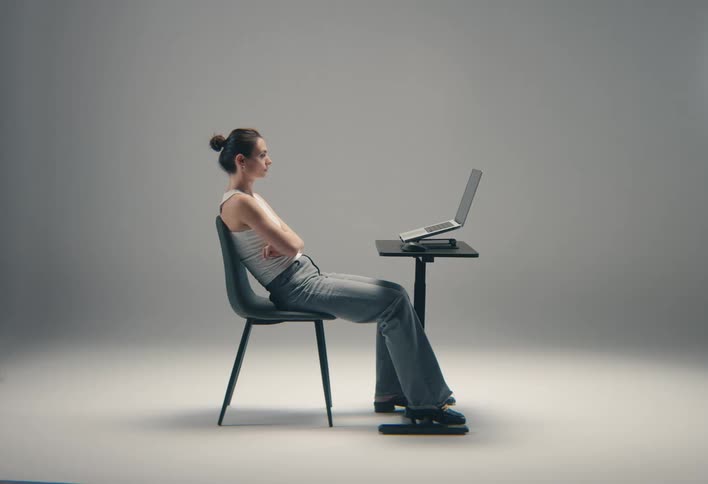 A woman sits with her laptop and nods during a video call in a brightly lit studio