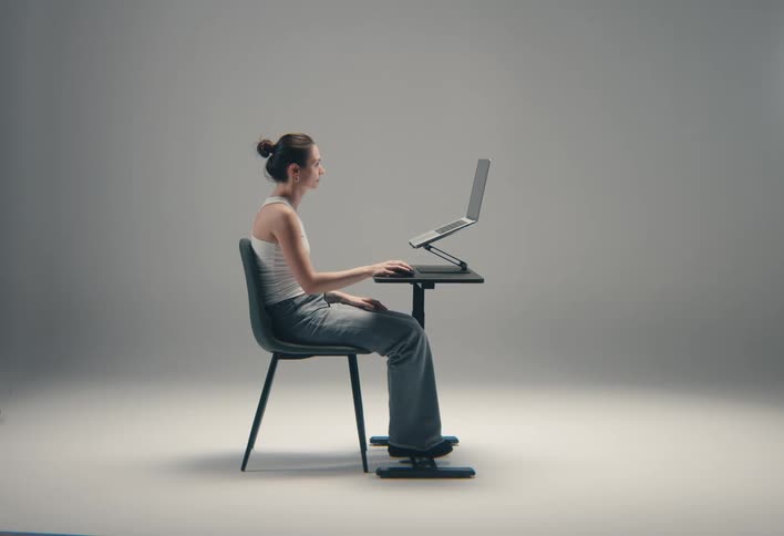 A female is sitting in front of a desk tray her body profile is facing the laptop