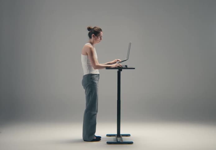 Woman standing at a table typing on a laptop computer