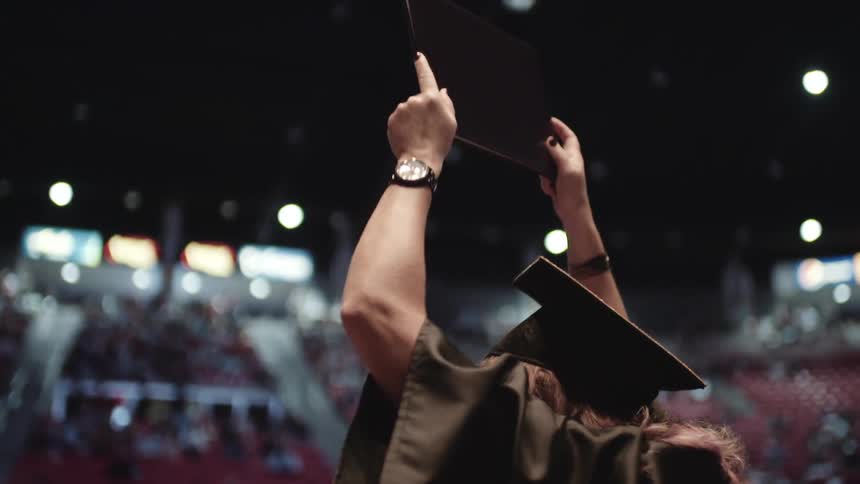 A woman raises a diploma at a graduation