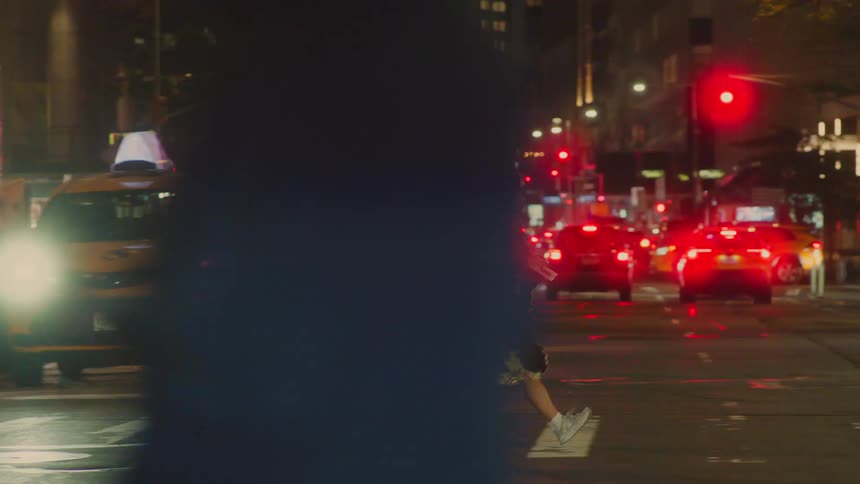 Person crosses a busy street at night with vehicles and city lights in the background