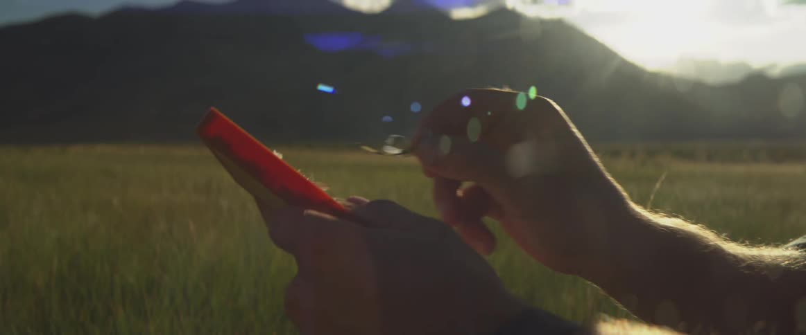 Hands holding rectangular object in an outdoor field