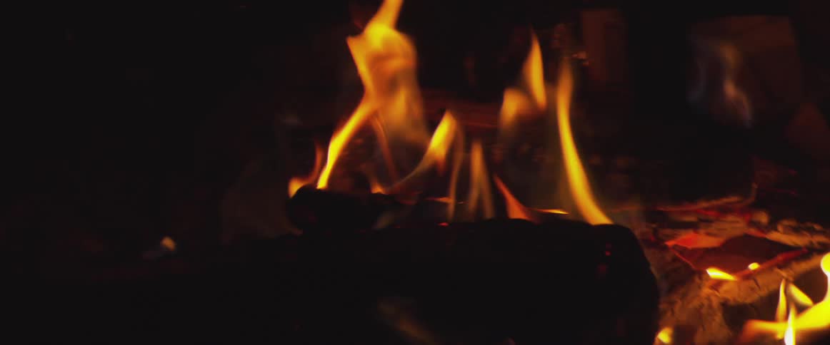 Flames and smoke rise from a wood fire burning in the dark