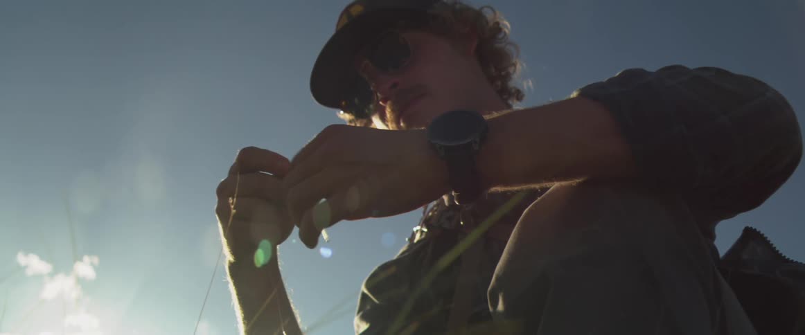 Fisherman half kneeling in the daytime ties a lure onto a fishing line
