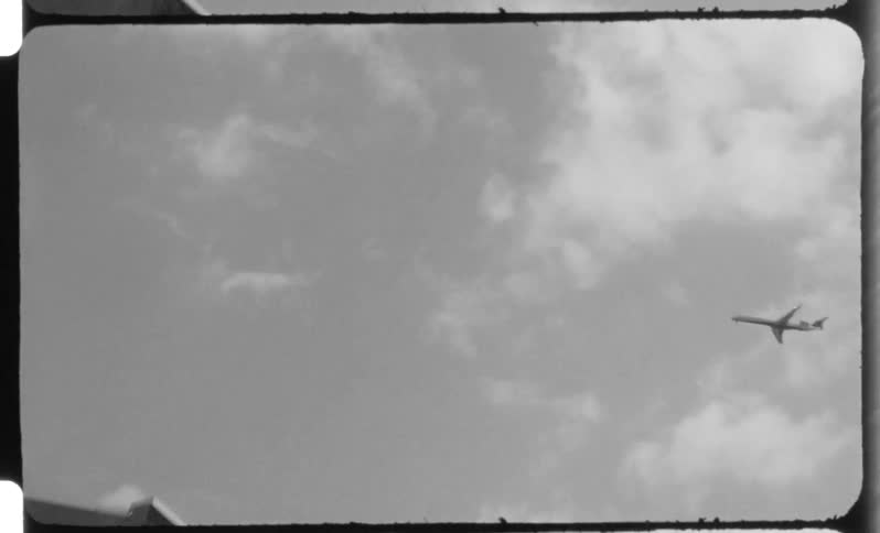 A highcontrast black and white shot of an airplane flying across a bright cloudy sky