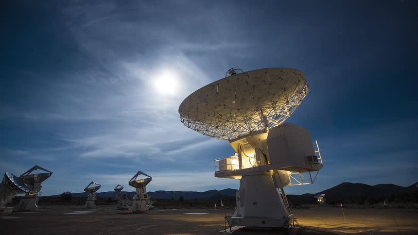 A group of radio telescope dishes point toward trolling clouds and a sky