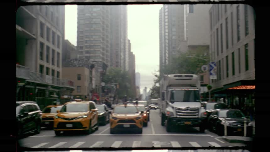 Yellow taxis and assorted vehicles crossing an intersection on a street lined with tall buildings