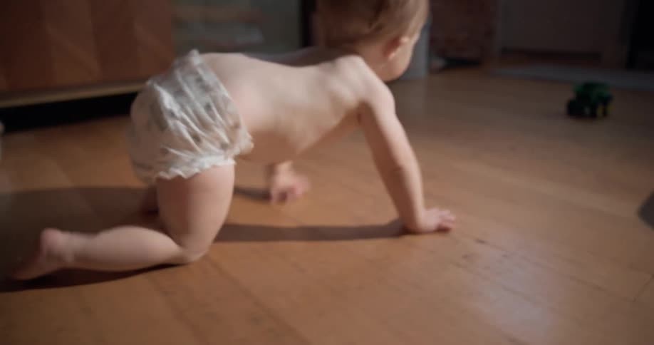 Baby wearing diapers crawling towards a toy car in a living room indoors during day time