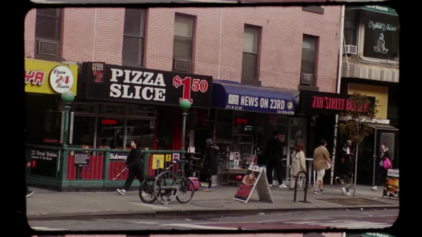 Several people walk past a pizza shop and subway entrance on a city street in a busy city