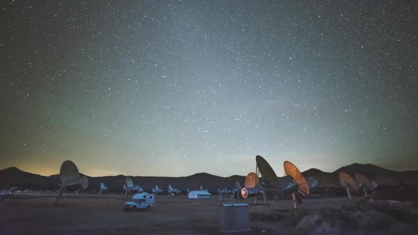 Camper moving away from satellite dishes in the desert as the stars of the milky way move across the sky