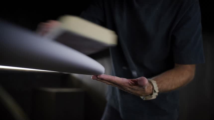 Man moving a sanding block along the elongated surface of a board