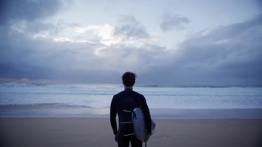 Surfer wearing a wetsuit holding a board while looking at the ocean