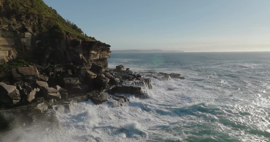 Sea waves breaking against a rocky cliff next to the sea outdoors during day time