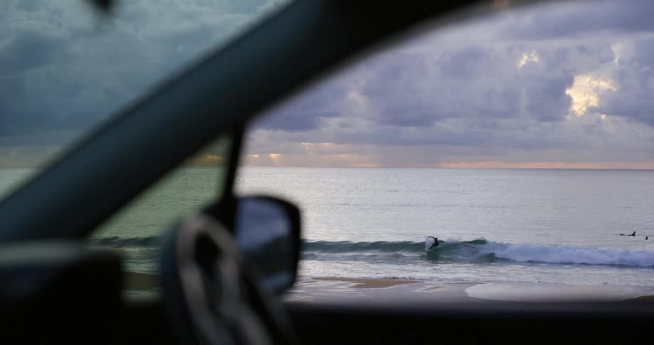 Surfers riding waves seen from inside a car