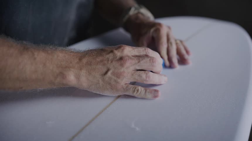 A man smooths down a surfboard