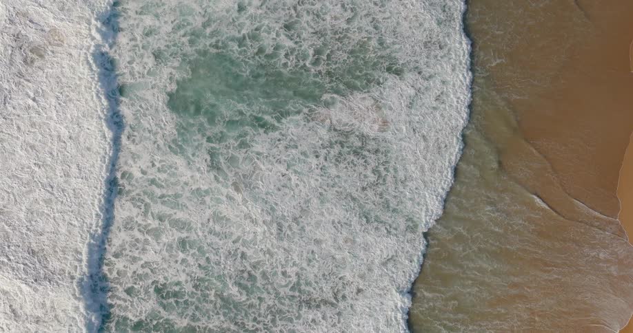 Aerial view of waves rolling in to shore and over sand on the beach
