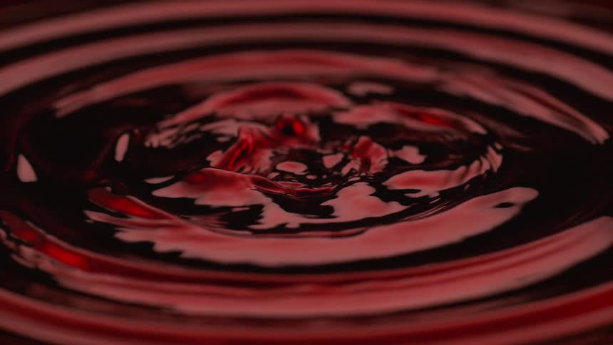 A mesmerizing slowmotion closeup showcases a dark liquids surface illuminated by red light vibrating intensely to form intricate repeating patterns and tall turbulent columns of splashing fluid