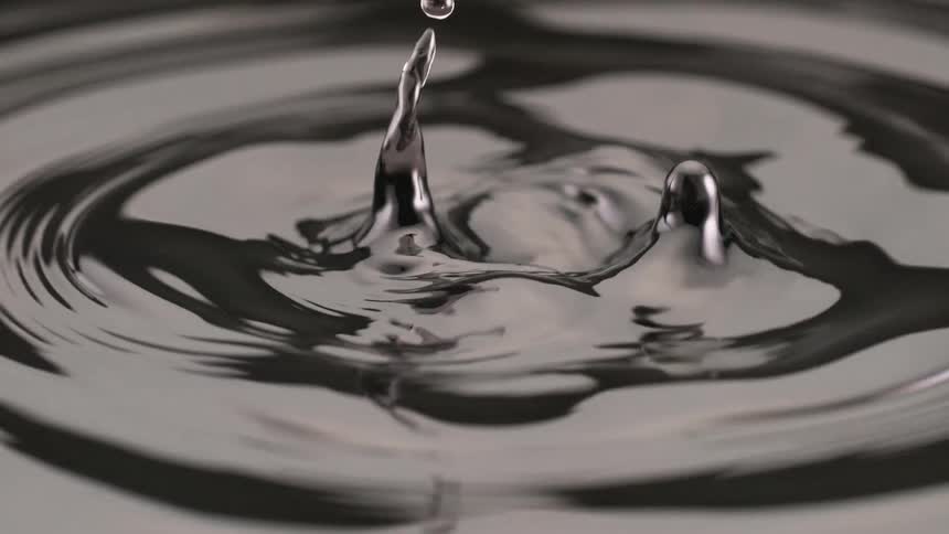 Gray liquid forming peaks and a droplet suspended above the rippled surface