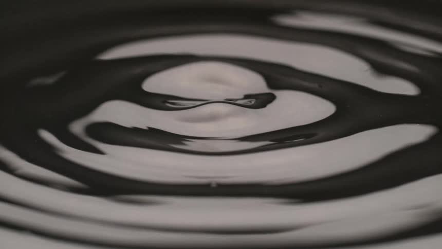 A black liquid starts out with circular ripples then it begins to pop up with bubbles and splashes