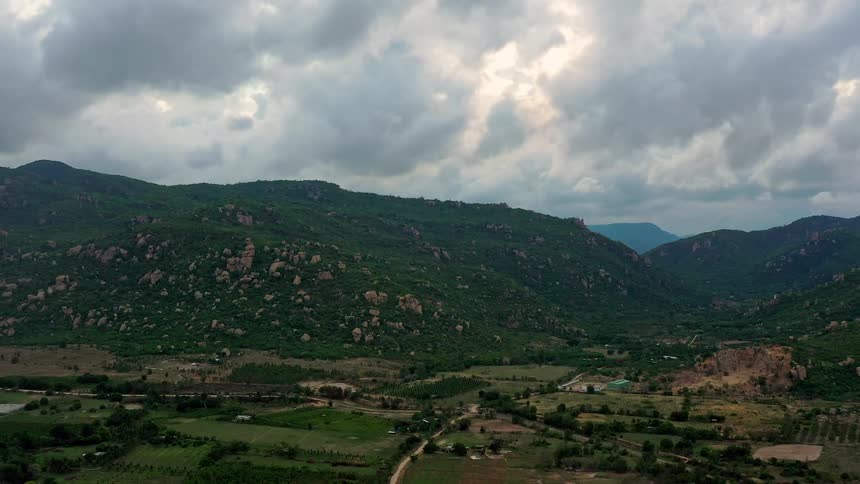 Agricultural valleys surrounded by green mountains with rocky outcrops under a cloudy sky