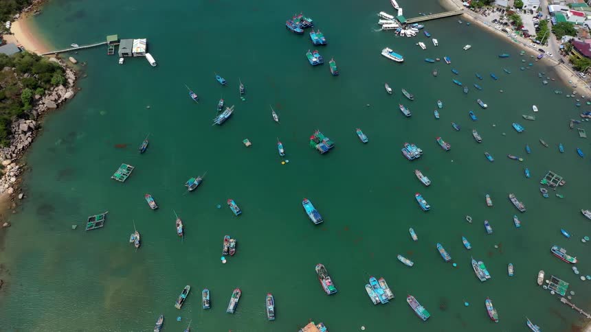 A series of boats sit docked on a calm lake beside a coastal town the midday sun casting bright light across the water and highlighting the shoreline buildings