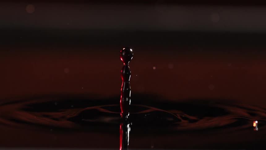 A mesmerizing macro slowmotion shot captures a single droplet impacting a dark liquid surface creating a splash crown that transitions into a high vertical rebound jet and rhythmic concentric ripples