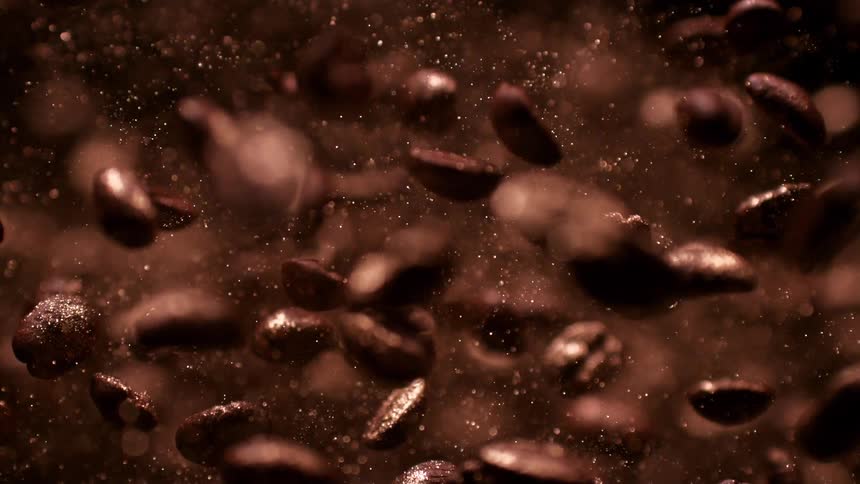 Dark coffee beans suspended among fine dispersing particles