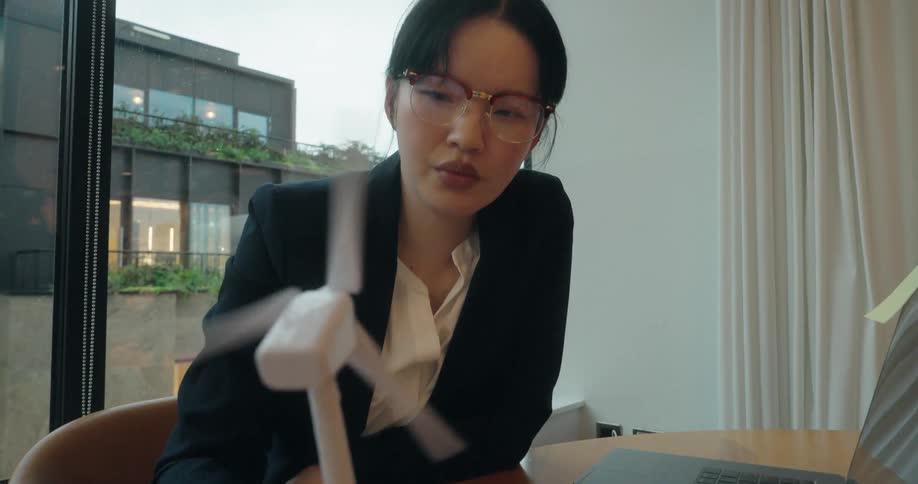 Woman in a suit interacts with a small wind turbine model on the table beside a laptop