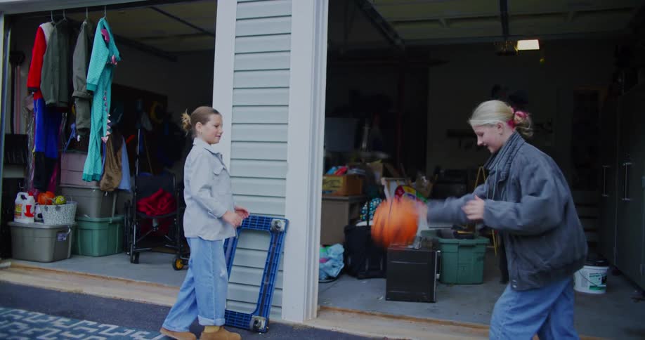 Two young girls play basketball outside a cluttered residential garage