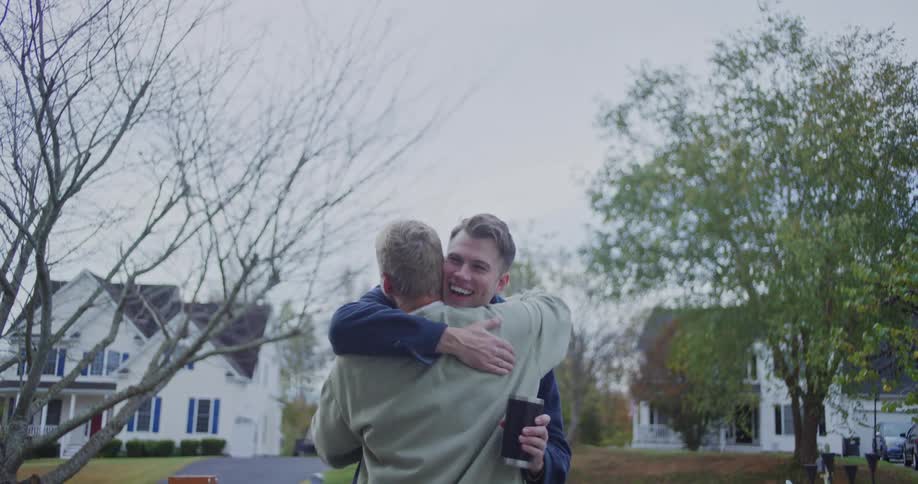 Men hug on a residential street while one of them holds a cup