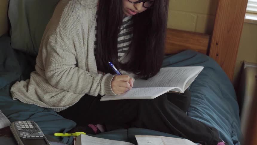 A girl is doing homework in a bedroom
