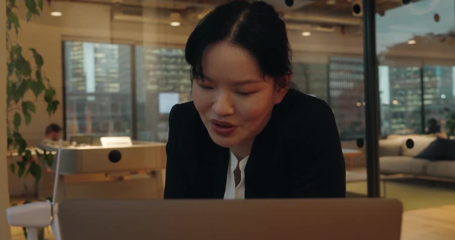 Woman sitting in an office after dusk participates in a conference call on her laptop