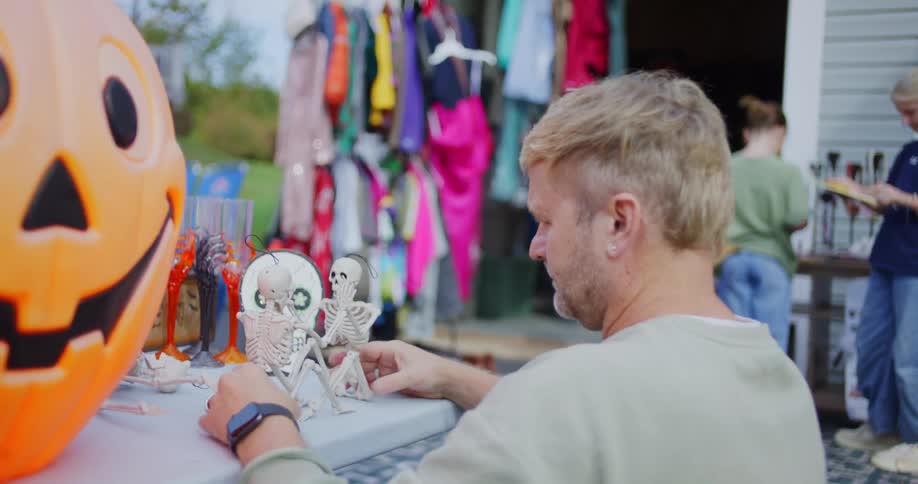 A man examines small skeleton figurines on a table at a yard sale