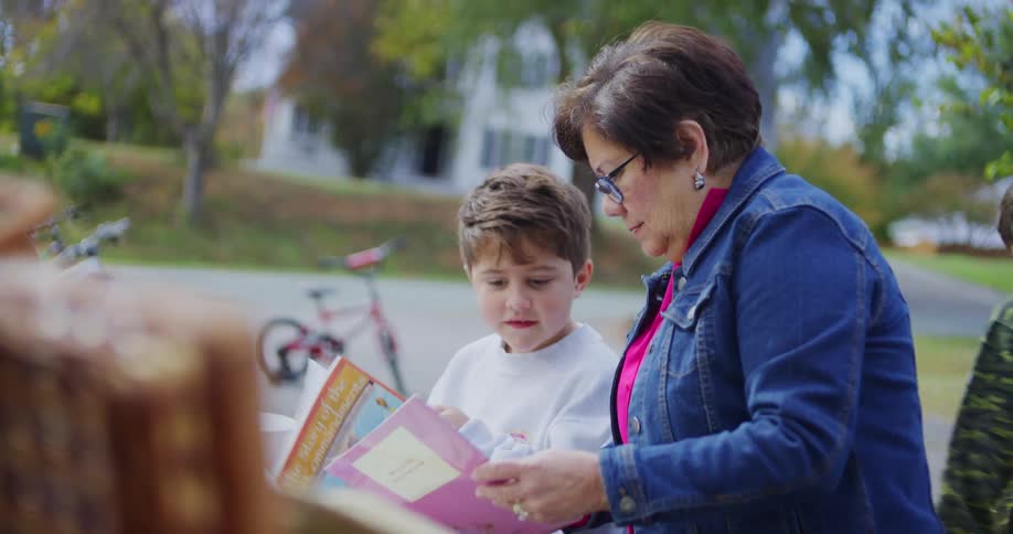 A woman and a young boy browse a colorful book at an outdoor garage sale