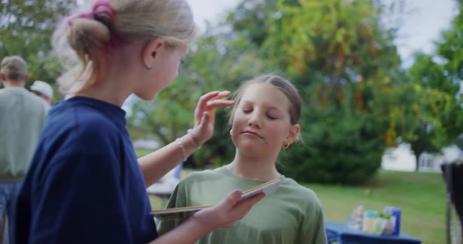 Child applies makeup to anothers face while holding a palette